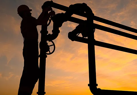 Worker silhouetted against a sunset on bore field pipework